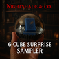 Hand holding a glass sphere with a blue cube inside, labeled '6-Cube Surprise Sampler' by Nightshade & Co.
